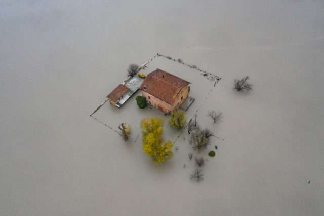 Aerial shot of a house with a fence in the middle of a flood.