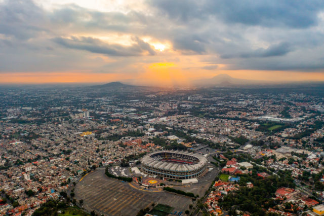 Aerial view of Mexico City with a soccer stadium in the middle of sprawling houses.