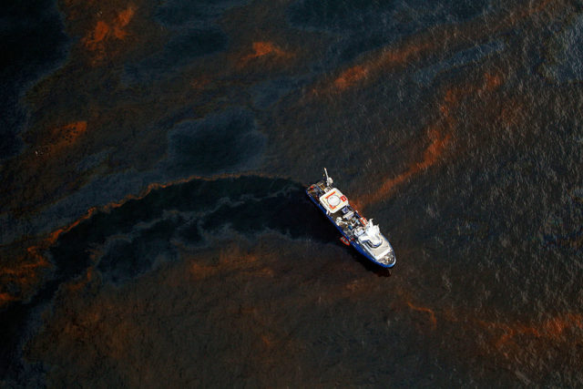Aerial view of a boat sailing through an oil spill.