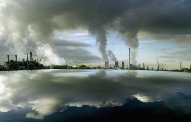 Oil refinery smoke stacks beside a body of water.