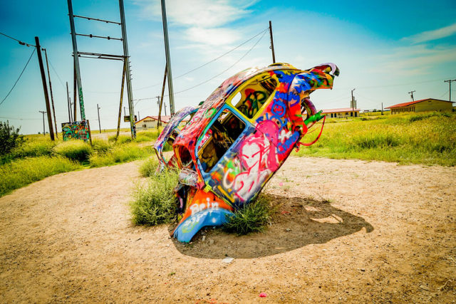 Spray painted Volkswagen Beetle buried nose first in the ground.