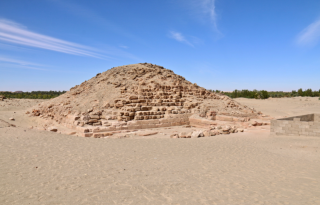 Pyramid of Nastasen with crumbling bricks, located in the desert in front of a blue sky.