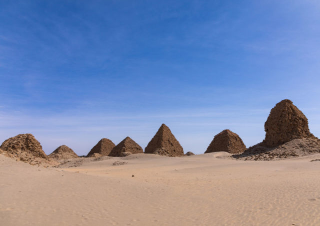 Numerous pyramids in a row in a sandy desert with a blue sky.