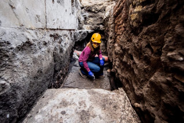 A woman in a hard hat standing on stone slabs in a hole