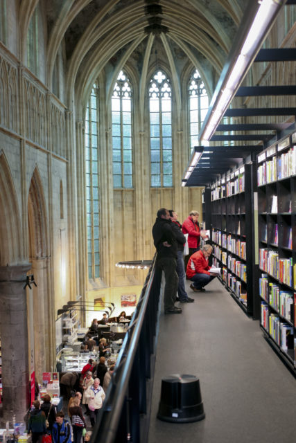 People looking at books on a shelf inside a church with domed roof