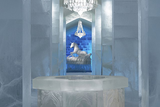 Room with a table made from ice positioned in the middle and a unicorn statue in the distance