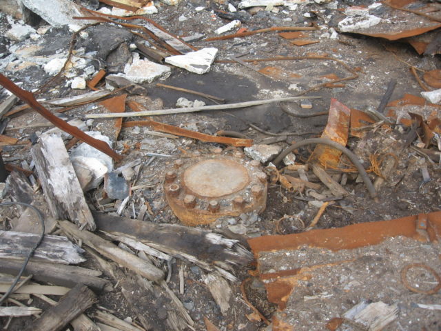 A metal cover is sealed over the Kola borehole, surrounded by the rubble of abandoned buildings