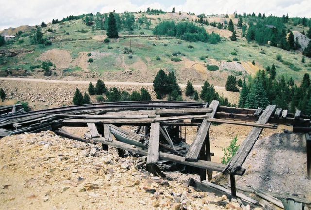 Wooden tracks used for ferrying gold falling apart, with a green hill in the background.
