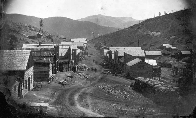 Black and white photo of Nevadaville in 1860 with log houses lining a dirt road.