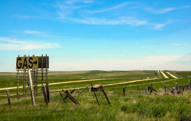 Yellow gas sign with an arrow in front of a long road that goes off into the distance.