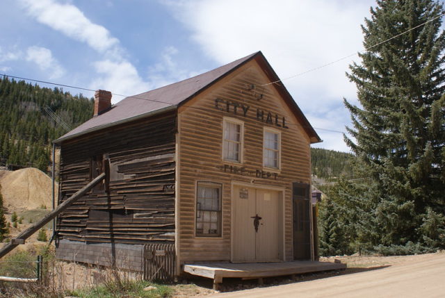 Wooden building with sign reading "City Hall; Fire Dept." 