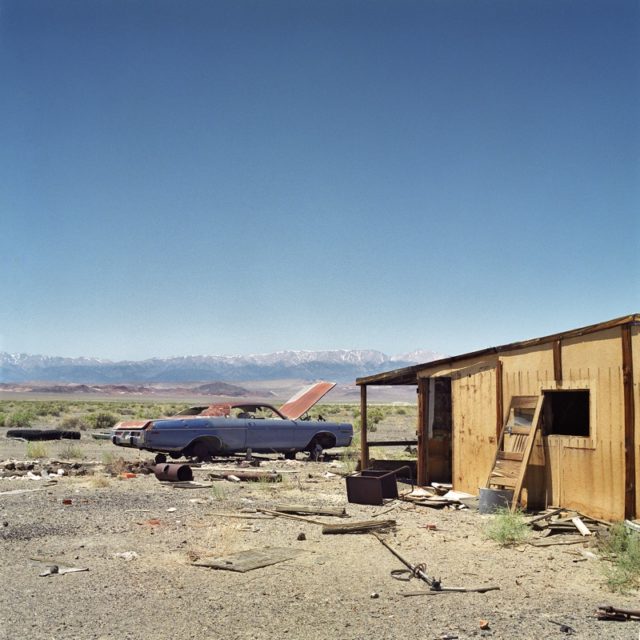 Abandoned car parked beside a wooden structure in Coaldale