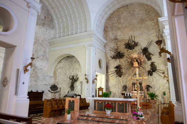 Interior of chapel with white arched ceilings and walls made of stone with an altar in the centre. 