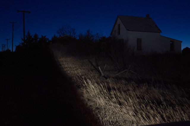 Old farmhouse in the dark with trees surrounding it.