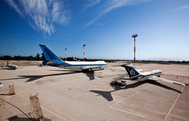 Two large airplanes and a third smaller on the the pavement at Ellinikon International Airport with a blue sky overhead.