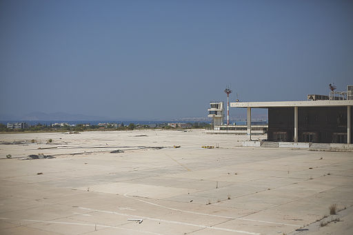 Pavement at Ellinikon International Airport with the air traffic control tower in the distance, with the water and mountains past that. 