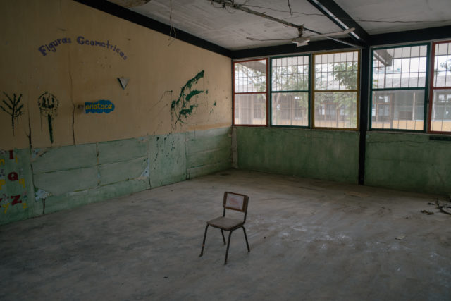 A chair sits abandoned in a room with decaying walls and large windows
