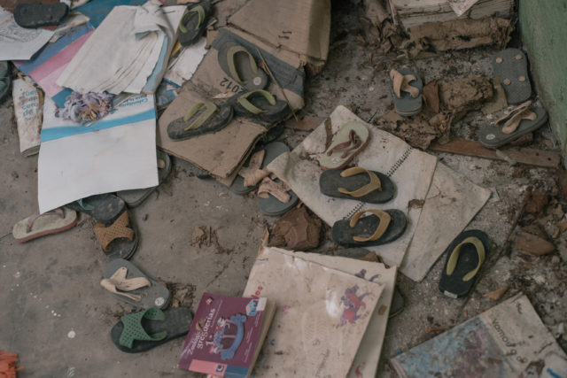 Sandals, cardboard, and debris on the floor of an abandoned room