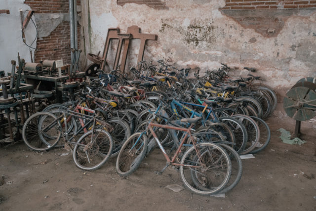 Several rusted bikes leaning against each other, up against a wall