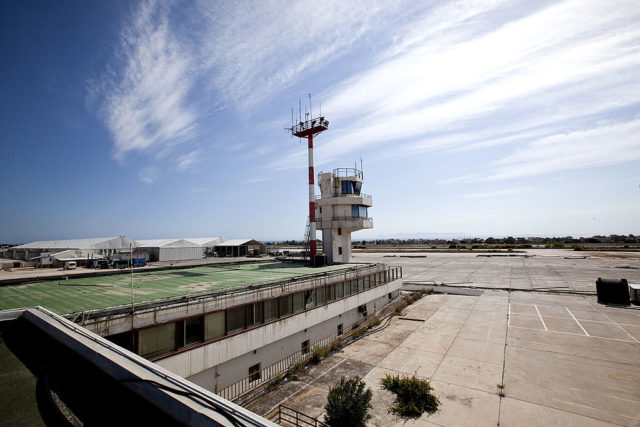 Air traffic control tower on top of a rusting building overlooking an airfield.