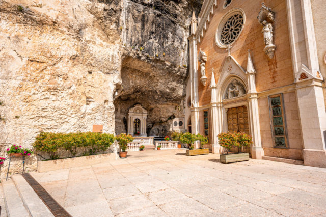 Front courtyard at Santuario Madonna della Corona with a shrine carved into the rock face near the chapel entrance.