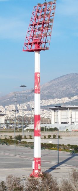 Tall red and white light tower in front of airport pavement.