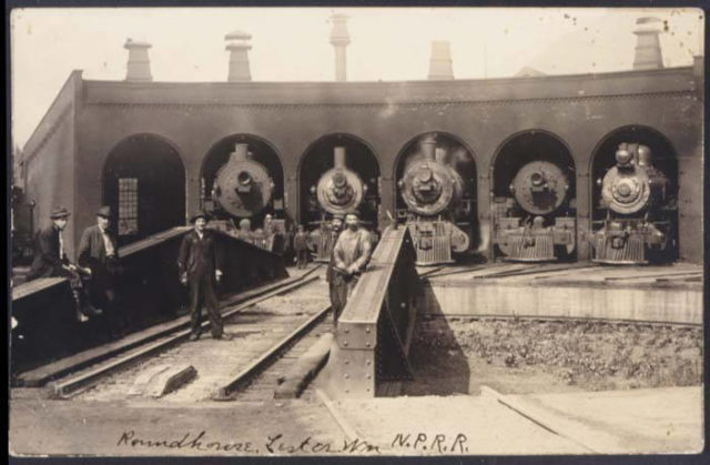 Steam-engine trains stations inside a rail station with men in front