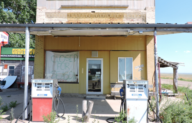 Decrepit yellow gas station with two pumps outside and a sign in the window reading "Closed for Season"