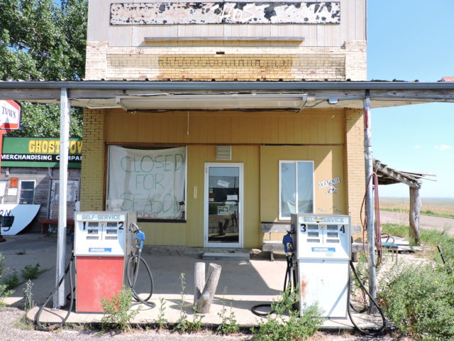 Decrepit yellow gas station with two pumps outside and a sign in the window reading "Closed for Season"