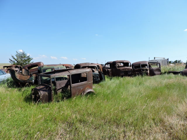 Darkly rusted abandoned cars in a field.