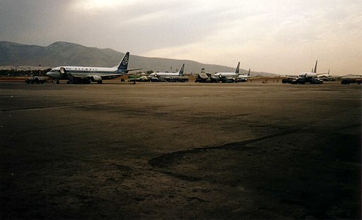 Row of airplanes lined up on pavement with mountains in the background.
