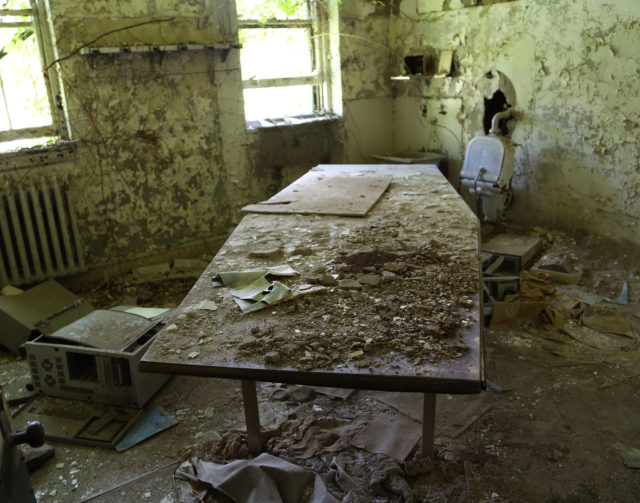 A medical table covered in dirt and debris in an abandoned room