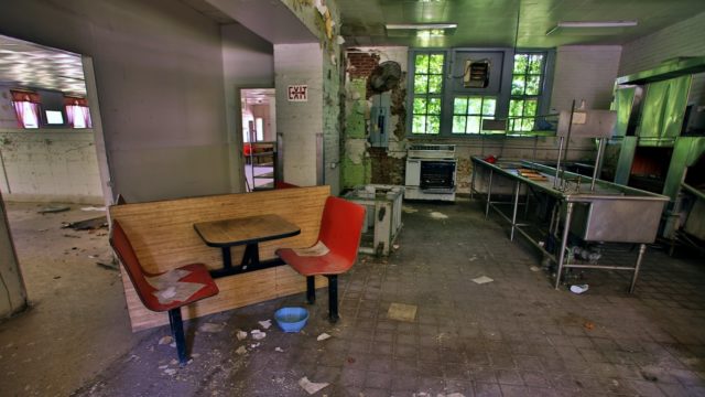 An abandoned and destroyed cafeteria area with a stove and countertops