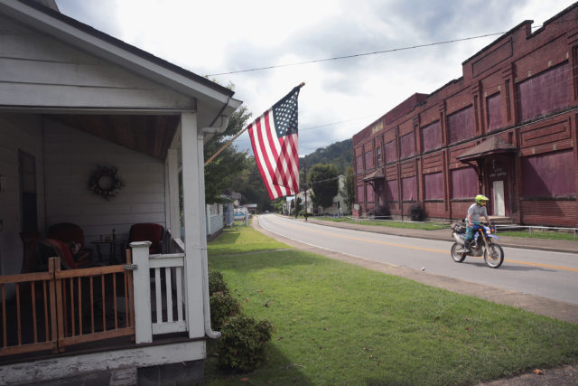 Dirt bike driving past a house with an American flag on its exterior