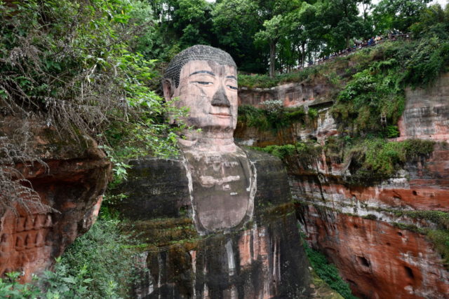 Giant Buddha head situated between trees and cliffs.