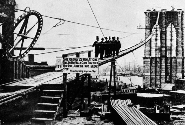 Men standing next to a warning sign during the construction of the Brooklyn Bridge