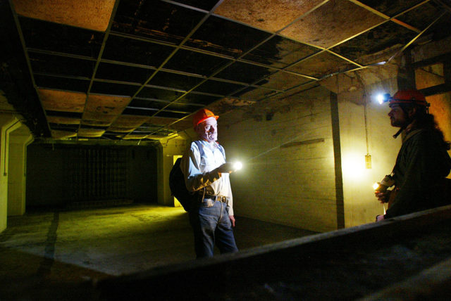 Men standing in a large underground room with flashlights