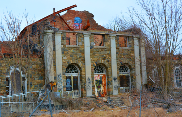 The front of an abandoned building with graffiti and damages