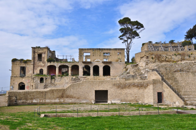 Ancient Italian villa with arched windows and green grass in front of a blue sky.