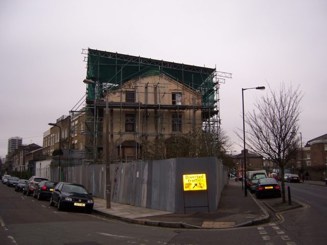 A decaying corner house with larges scaffolding surrounding it