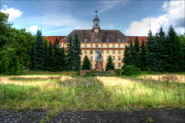 Large abandoned building with trees surrounding it. 