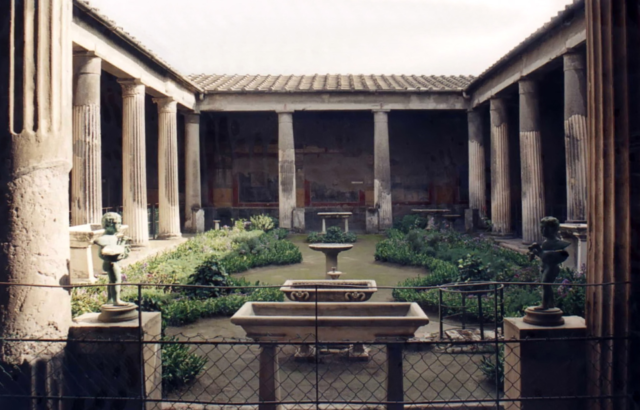 A view of the garden at Casa dei Vettii, with benches, statues, greenery, and a fountain.