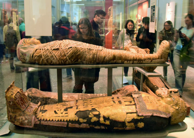 Visitors look into a glass case with two mummies on display.