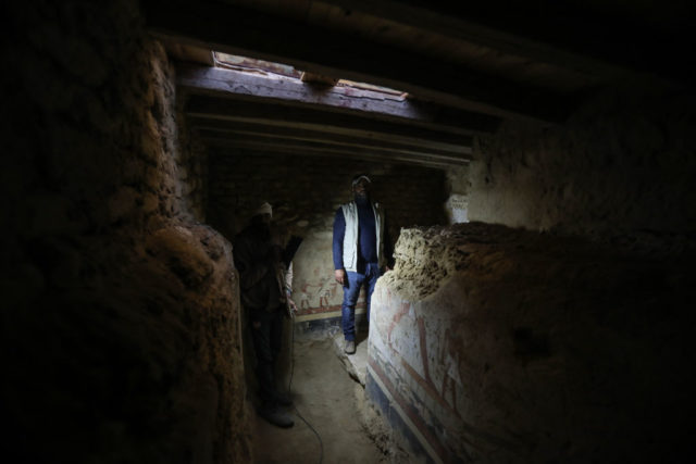 Man standing in a dark room with a large sarcophogus in the middle.