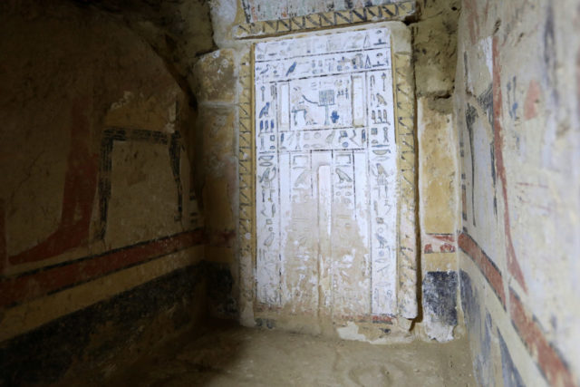 Interior of an Egyptian tomb with a large white slab of inscriptions on the wall.