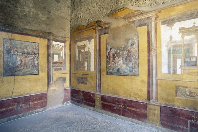 The corner walls of a room with tattered frescoes painted on them