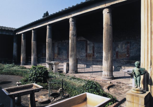 Pillars holding up a roof with a garden in front, a small statue stands