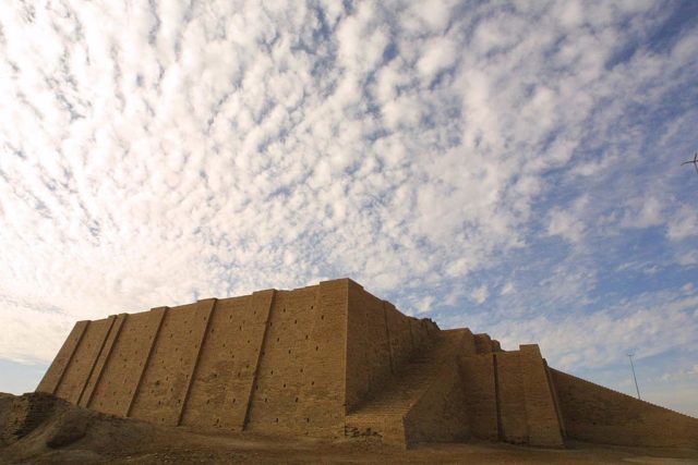 Distanced view of the Ziggurat of Ur in front of a cloudy, blue sky.