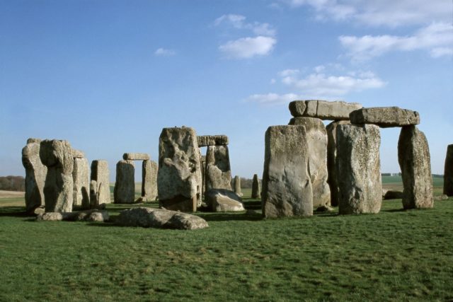 Stonehenge in a green field with bright blue sky.