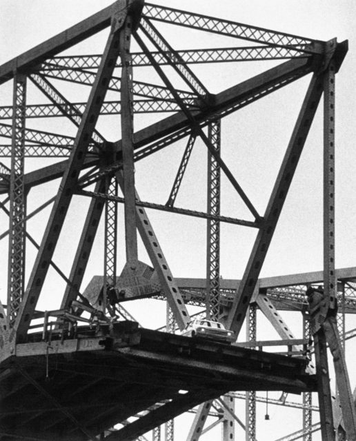 An opening of a bridge that had collapsed, a car sits on the edge.